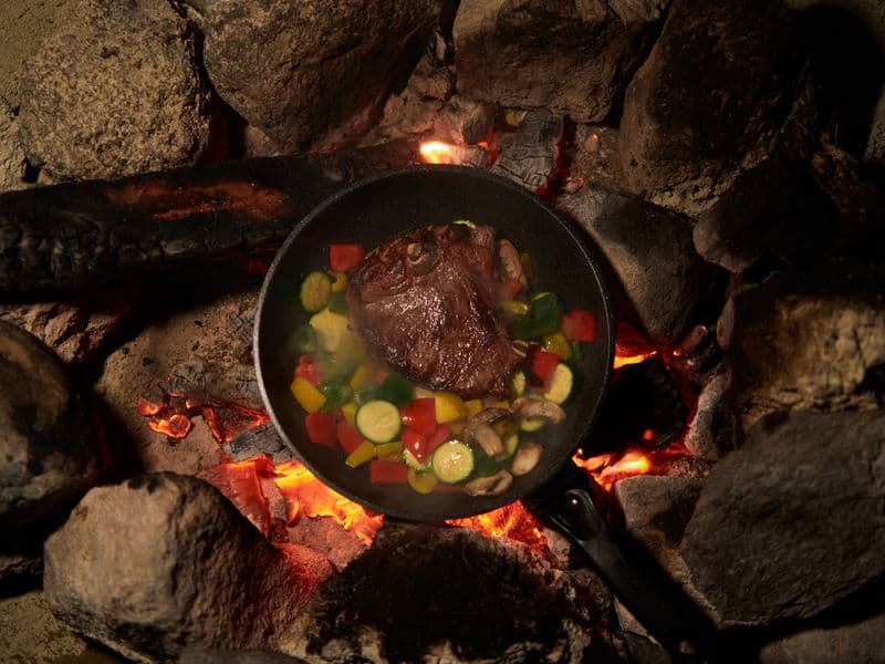 A beef steak cooking with vegetables over heat