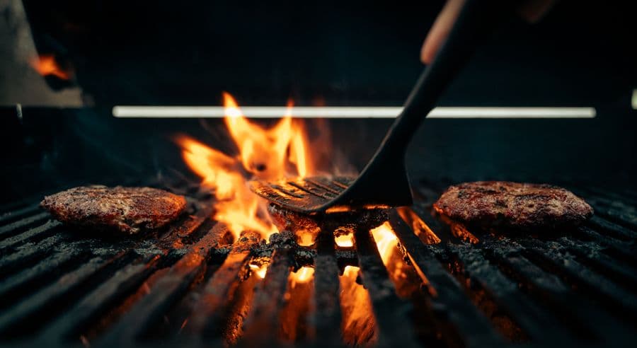 Beef patties sizzling over a flaming grill