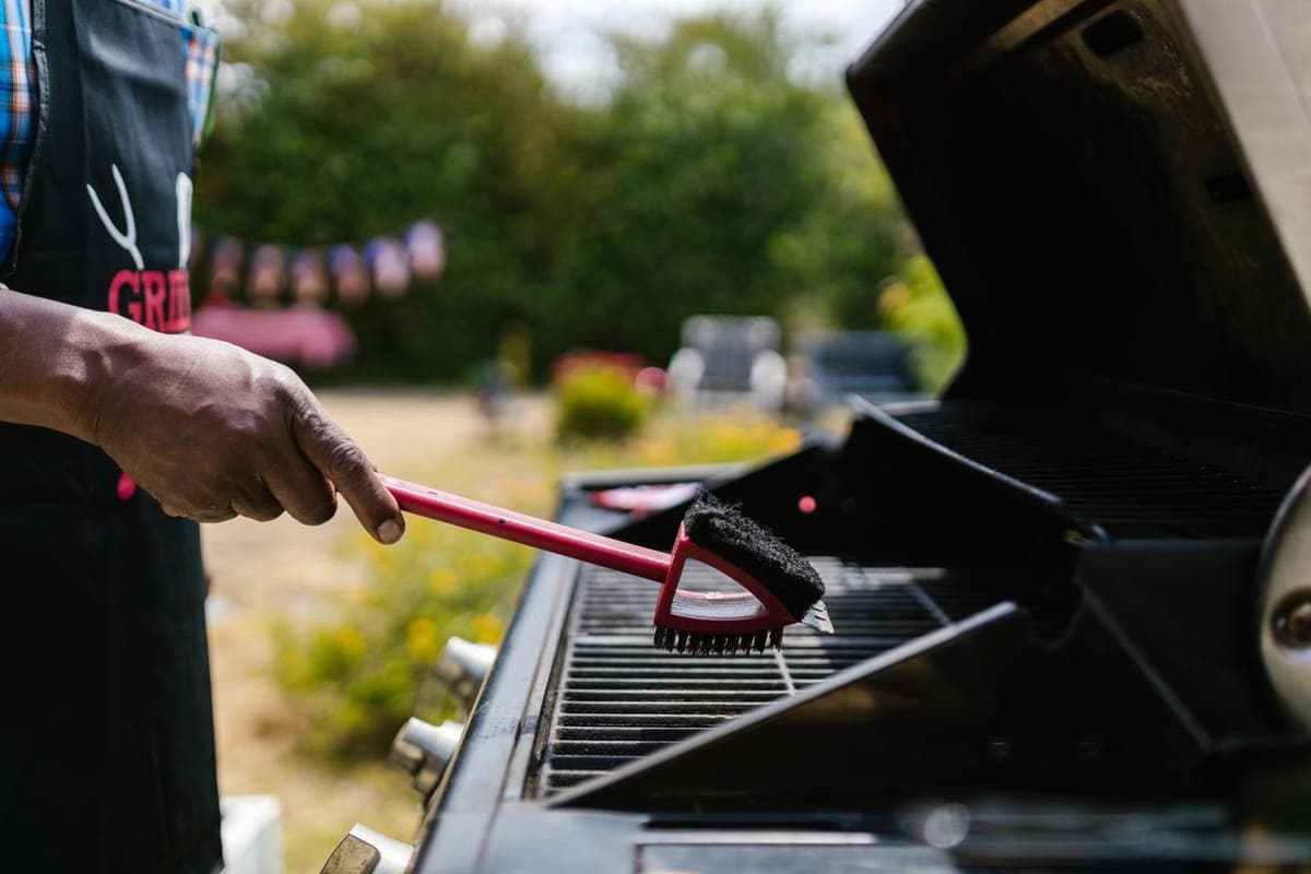 A person cleaning a barbecue grate with a brush