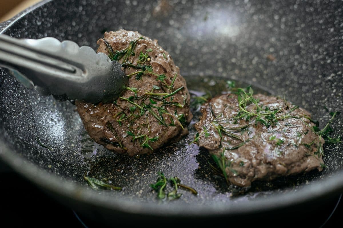 Seasoned cutlets frying in a hot pan with metal tongs
