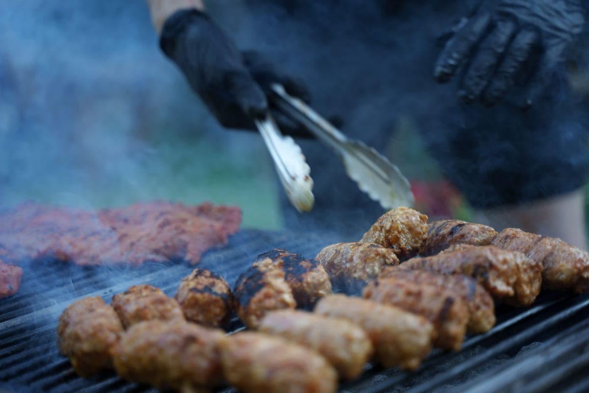 Tongs turning meat on a grill with smoke rising