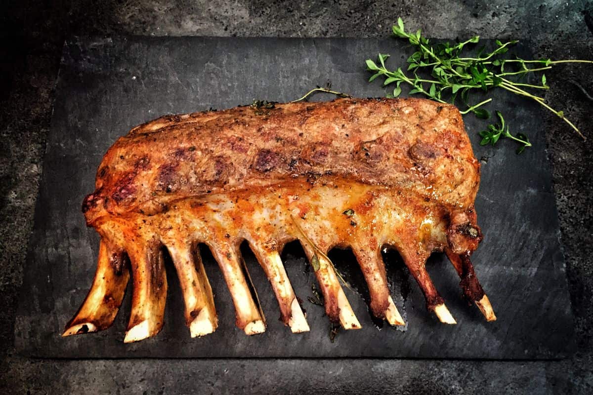 Grilled spare ribs resting with fresh herbs on a stone surface